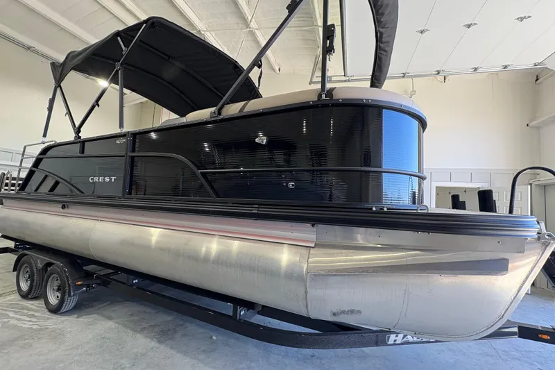 Slide: The Image of 2025 Crest Classic 220 pontoon boat in a showroom, featuring sleek black design. - 8