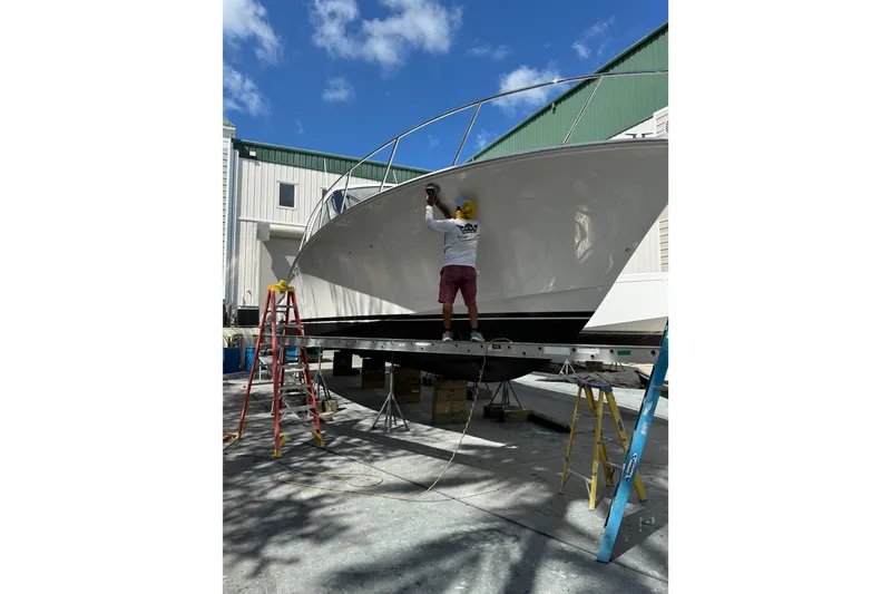 Slide: The Image of Worker maintaining a 2013 Cabo 44 Hardtop Express boat on a sunny day. - 108