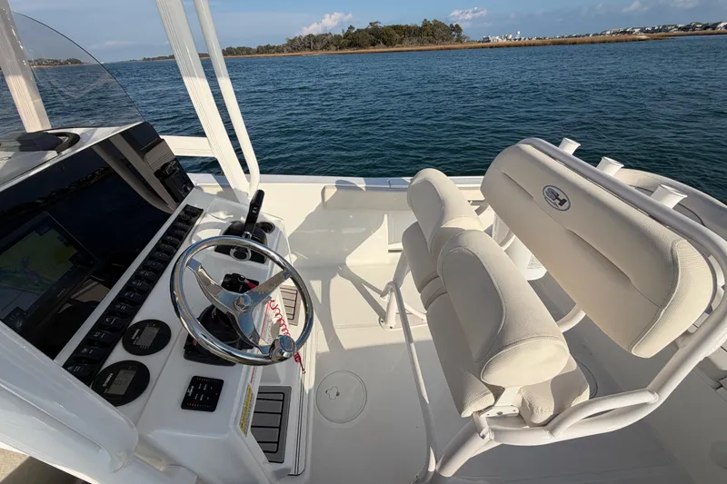 Slide: The Image of 2025 Sea Hunt Ultra 229 boat interior with steering wheel and seating, on calm water. - 32