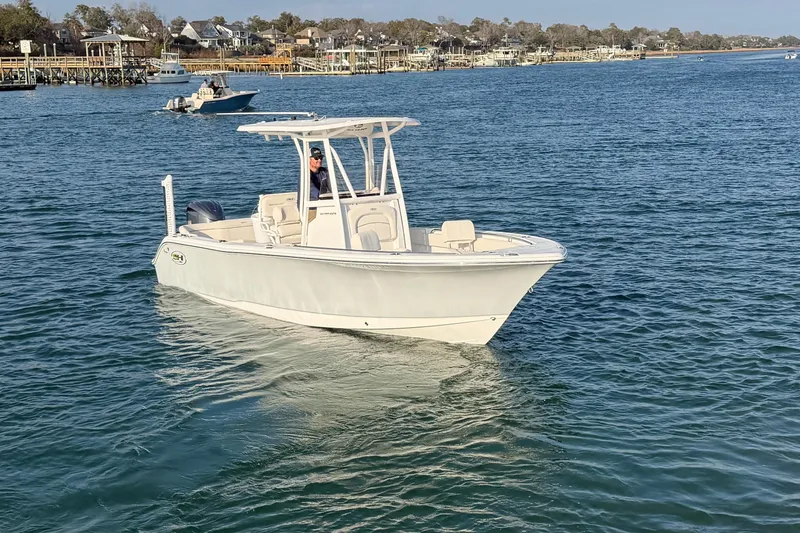 Slide: The Image of 2025 Sea Hunt Ultra 229 boat cruising on a calm lake near a residential shoreline. - 45