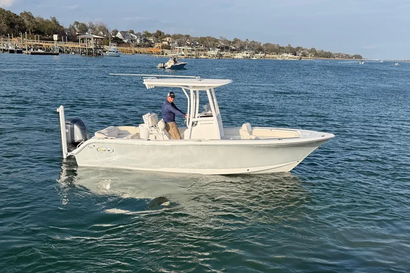 Slide: The Image of 2025 Sea Hunt Ultra 229 boat cruising on a calm blue sea near a coastal town. - 48