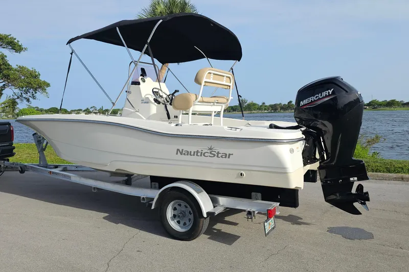 Slide: The Image of 2021 NauticStar 191 Hybrid boat on trailer with Mercury outboard motor by a lake. - 2