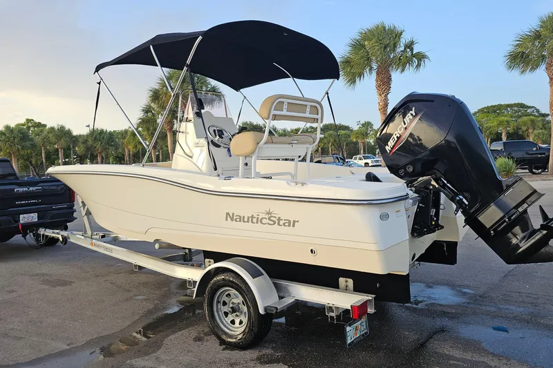 Slide: The Image of 2021 NauticStar 191 Hybrid boat on trailer with Mercury outboard motor, parked near palm trees. - 43