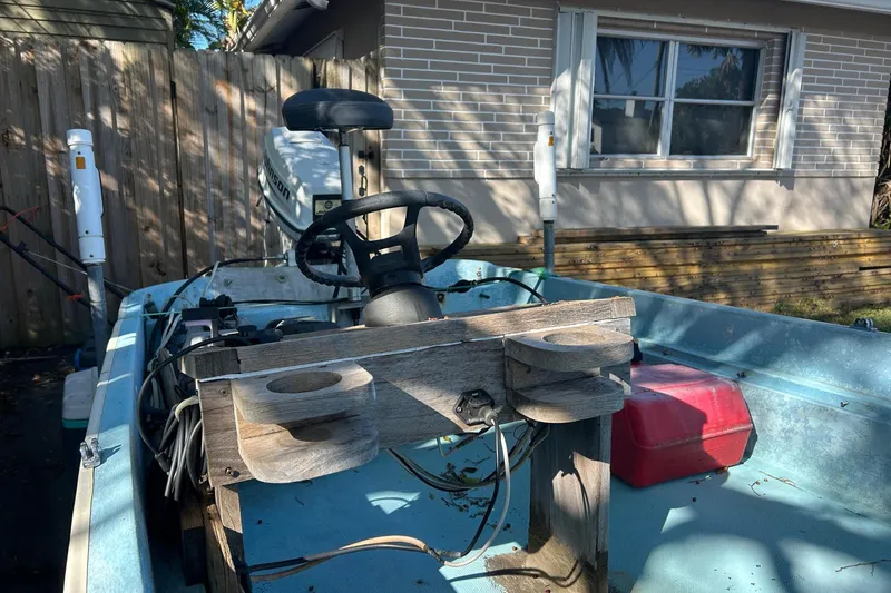 Slide: The Image of 1969 Boston Whaler 13 Sport boat interior with steering wheel and motor, parked near a house. - 13