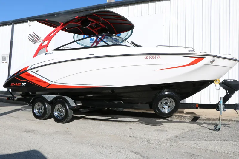 The Image of 2018 Yamaha Boats 242X E-Series on trailer, white with red accents, parked outdoors. - 1