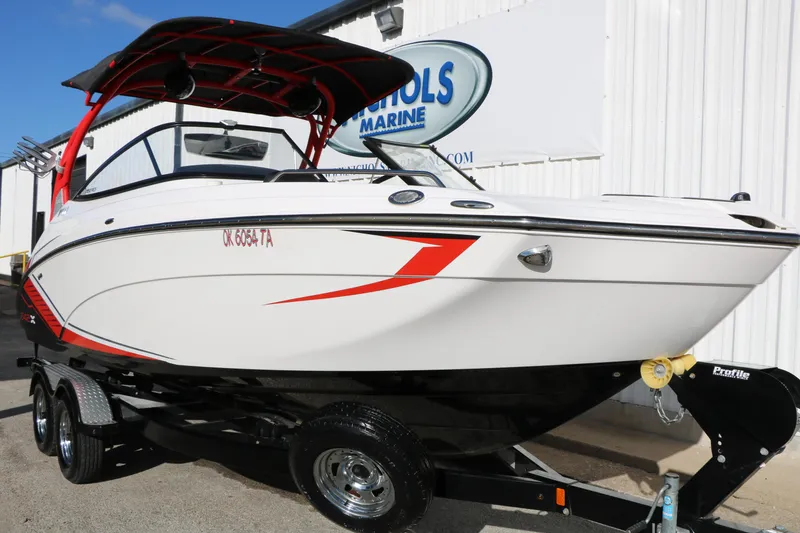 Slide: The Image of 2018 Yamaha Boats 242X E-Series on trailer, white with red accents, parked outdoors. - 3