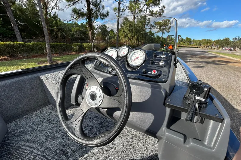 Slide: The Image of 2026 Tracker Pro 170 boat dashboard with steering wheel and gauges, surrounded by trees. - 9