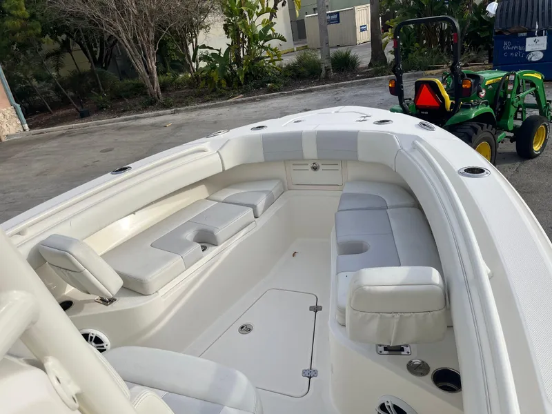 Slide: The Image of 2020 Mako 236 CC boat interior with white seating and cup holders, parked near greenery. - 12