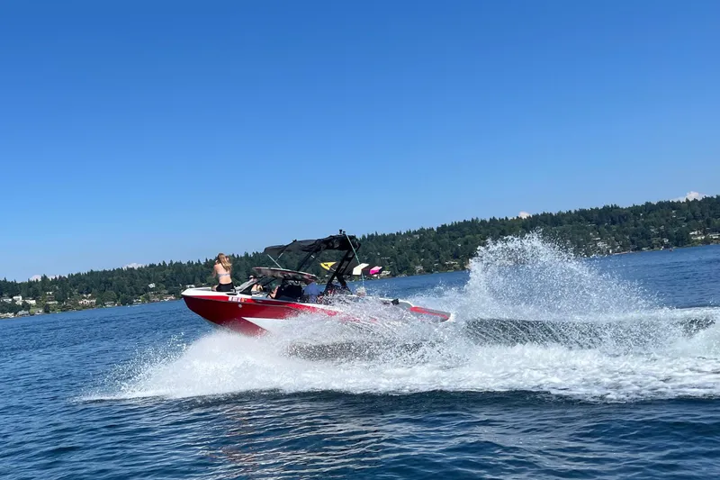 The Image of 2024 Axis T 220 boat speeding on a lake, creating splashes under a clear blue sky. - 14