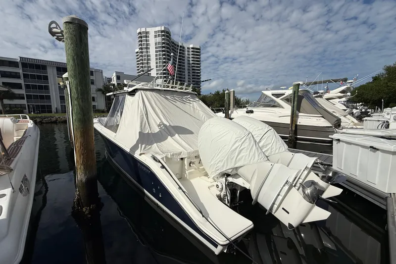 Slide: The Image of 2022 Pursuit S 358 Sport boat docked in marina, covered engines, modern buildings in background. - 14