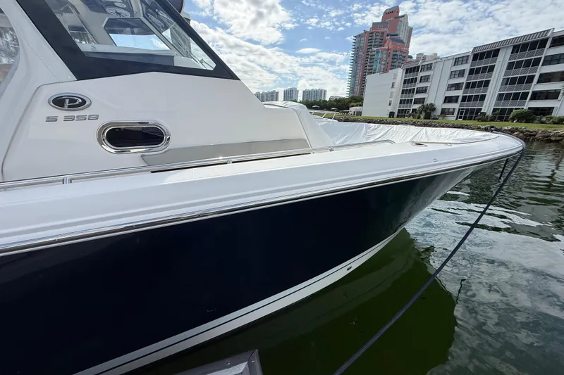 Slide: The Image of 2022 Pursuit S 358 Sport boat docked near waterfront buildings under a cloudy sky. - 18