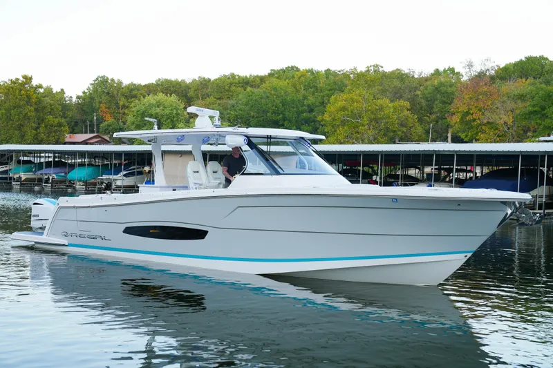 Slide: The Image of 2021 Regal 38 SAV boat docked on calm water with lush green trees in the background. - 1