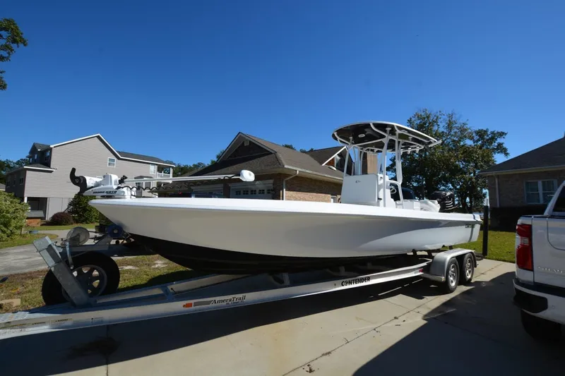 The Image of 2013 Contender 25 Bay boat on trailer in residential driveway under clear blue sky. - 1