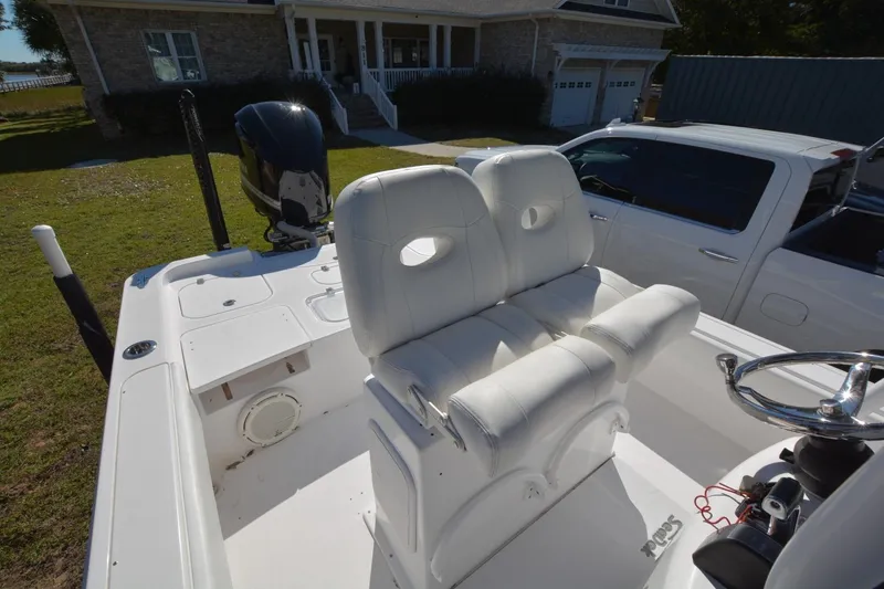 Slide: The Image of 2013 Contender 25 Bay boat with white seating and steering wheel, parked near a house. - 9