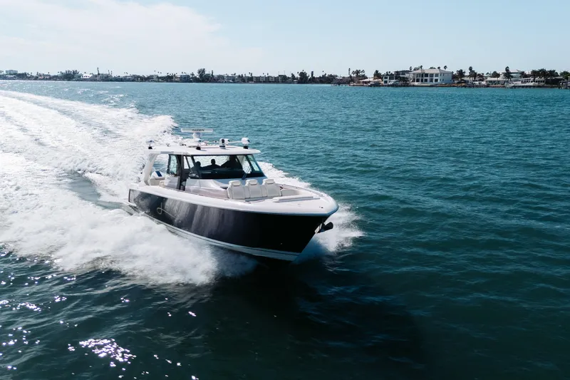 Slide: The Image of 2023 Tiara 48 yacht cruising on open water near coastal homes. - 10