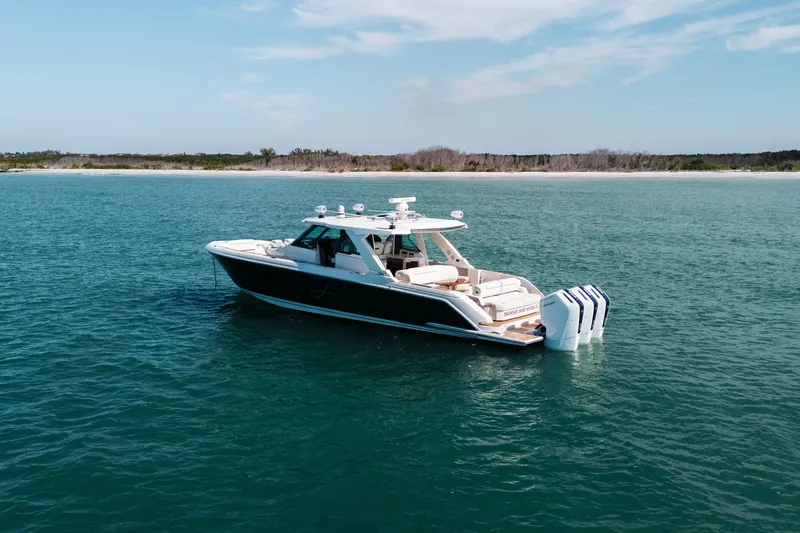 Slide: The Image of 2023 Tiara 48 yacht cruising on serene blue waters near a sandy shoreline. - 14