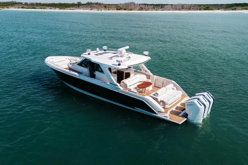 Slide: The Image of 2023 Tiara 48 yacht cruising on calm blue waters near a sandy shoreline. - 15