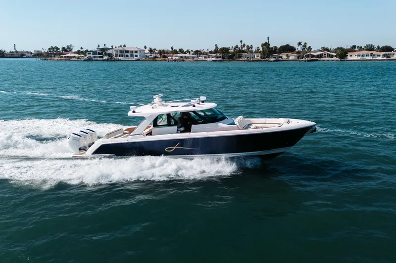 Slide: The Image of 2023 Tiara 48 yacht cruising on blue water near coastal homes. - 2
