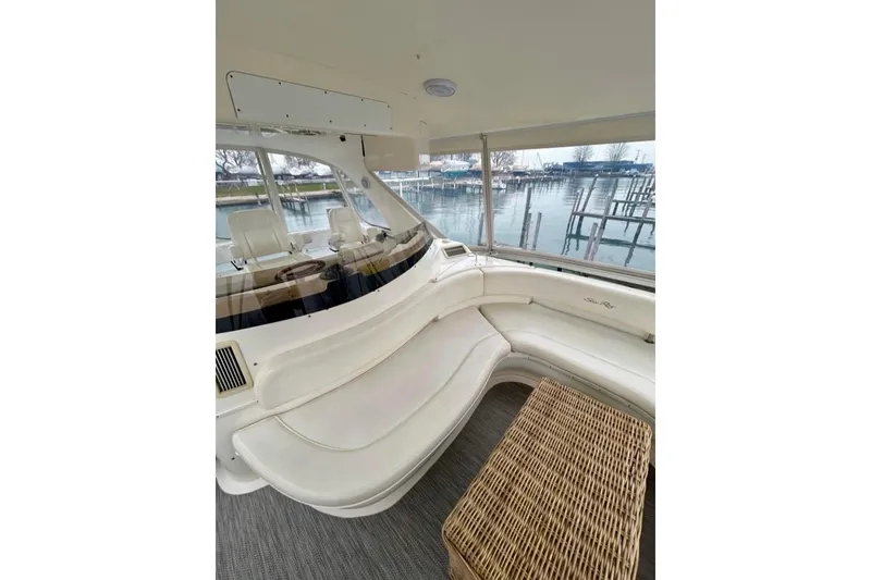 Slide: The Image of 2001 Sea Ray 560 Sedan Bridge interior with white seating and wicker table, overlooking marina. - 22