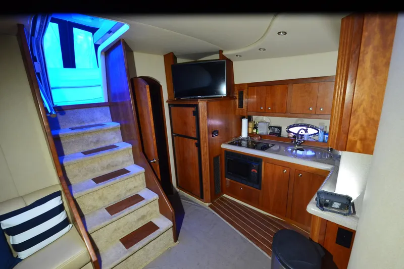 Slide: The Image of Interior of 2003 Cruisers Yachts 4370 Express with kitchen and stairs, featuring wood cabinetry. - 13