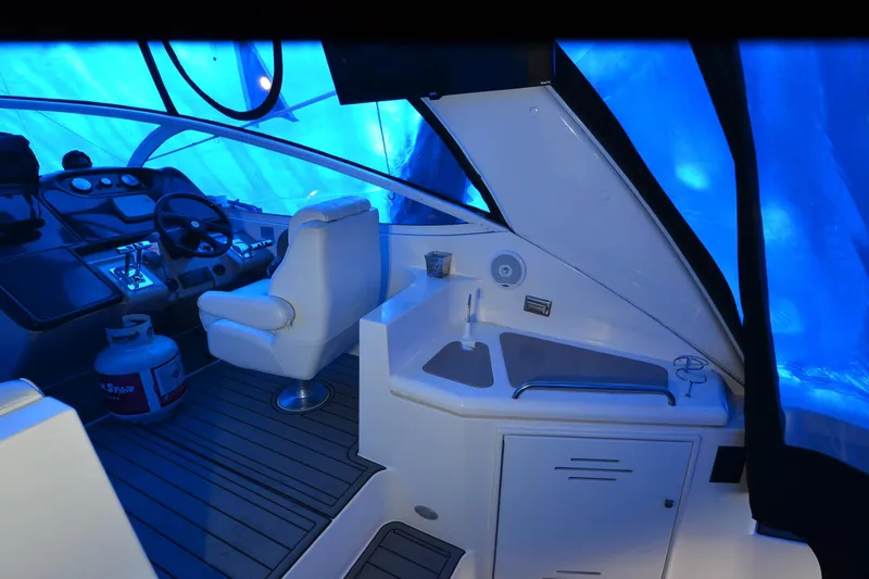 Slide: The Image of 2003 Cruisers Yachts 4370 Express cockpit with steering wheel, seating, and kitchenette under blue cover. - 33