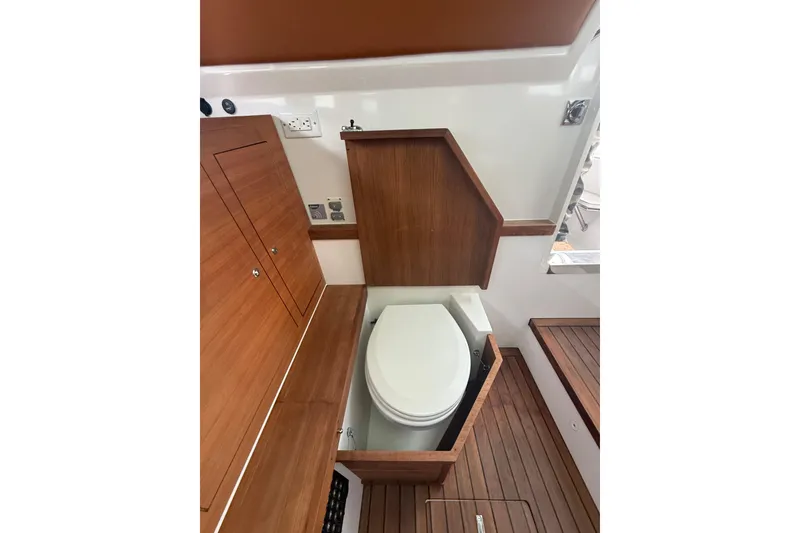 Slide: The Image of 2018 Axopar 37 Sun-Top boat interior with wooden cabinetry and compact toilet. - 14