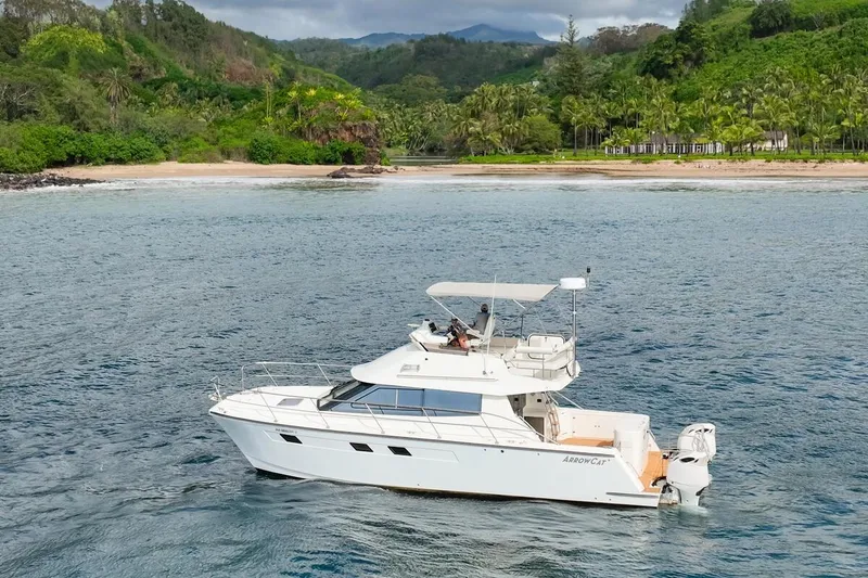 Slide: The Image of 2023 ArrowCat 420 Flybridge yacht cruising near a lush tropical shoreline. - 2