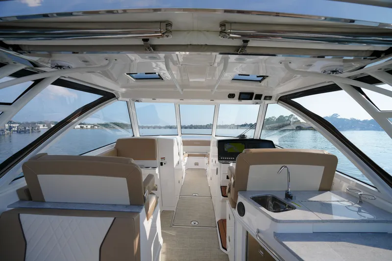 Slide: The Image of 2023 Everglades 340 Dual Console boat interior with seating and wooden table, overlooking calm water. - 3
