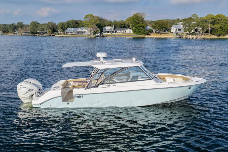 Slide: The Image of 2023 Everglades 340 Dual Console boat on serene water with scenic shoreline background. - 49