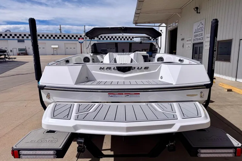 Slide: The Image of 2026 Nautique Ski Nautique boat, rear view, parked at a service entrance under a clear sky. - 5