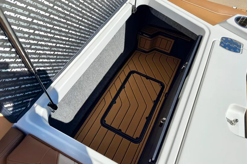 Slide: The Image of 2026 Nautique Super Air Nautique S21 storage compartment with brown flooring and branded cover. - 31