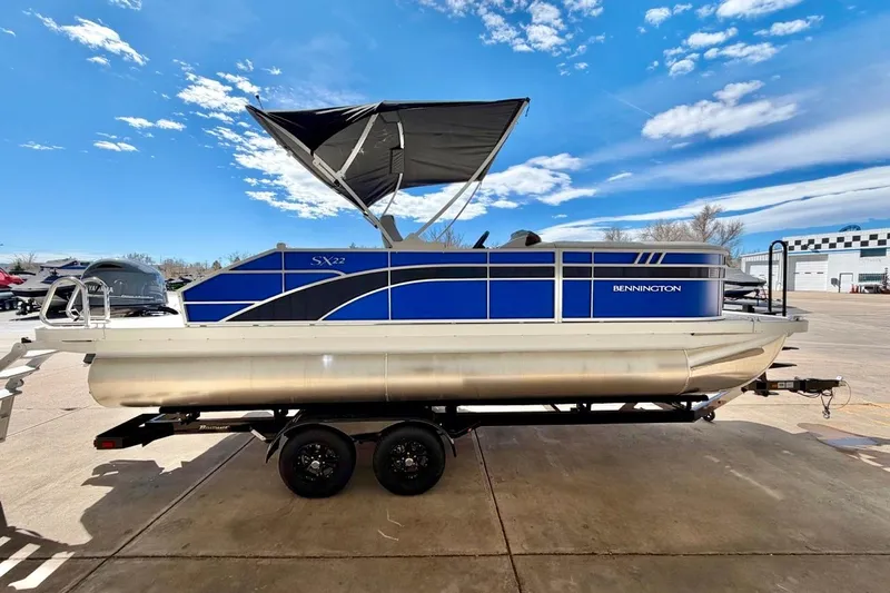 Slide: The Image of 2026 Bennington 22 SX Swingback pontoon boat with blue accents on a trailer. - 10