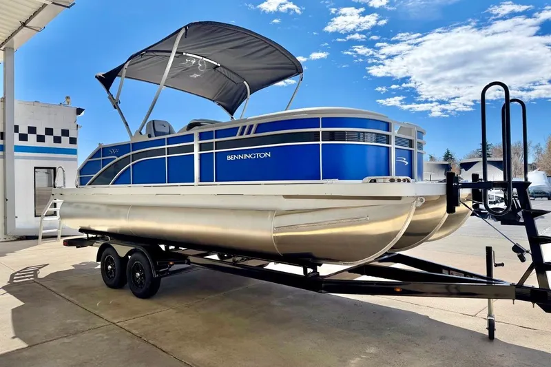 Slide: The Image of 2026 Bennington 22 SX Swingback pontoon boat on trailer under blue sky. - 11