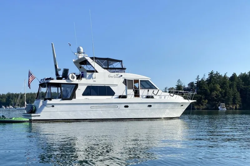 Slide: The Image of Compass 55 yacht from 2000 on calm water, surrounded by trees and boats. - 3