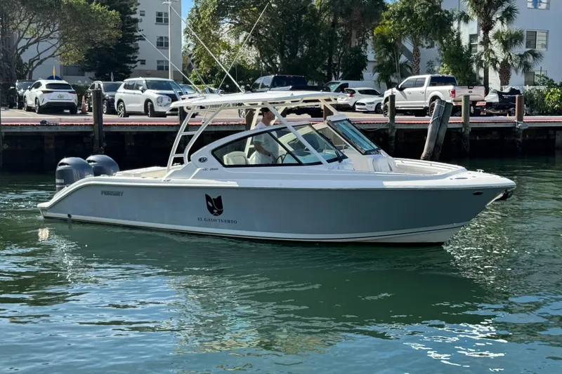 Slide: The Image of 2022 Pursuit DC 266 Dual Console boat docked in a marina, surrounded by parked cars. - 2