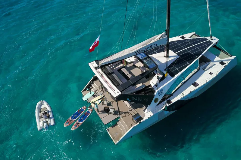Slide: The Image of 2024 Wave Wave60 catamaran sailing on clear blue ocean near a lush coastline. - 4