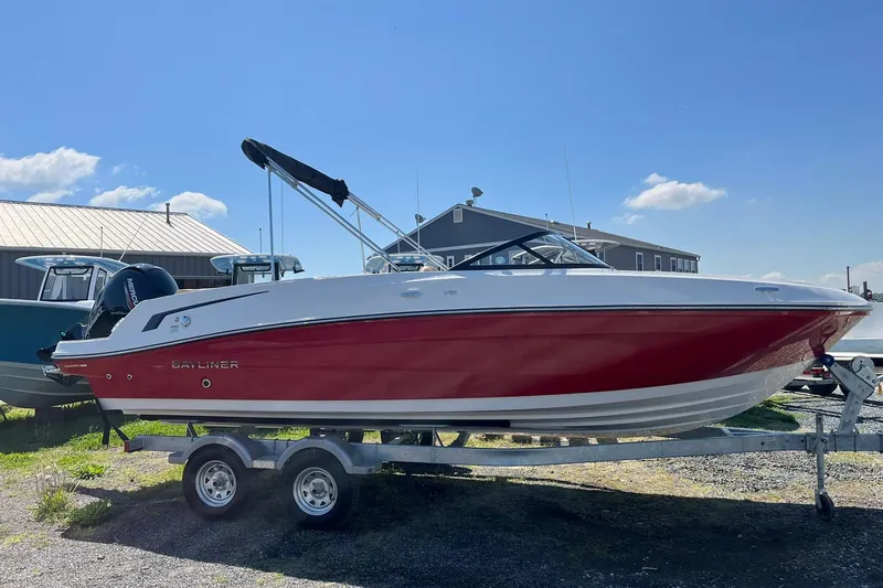 The Image of 2026 Bayliner VR6 Bowrider OB on trailer, red and white design, sunny day background. - 2