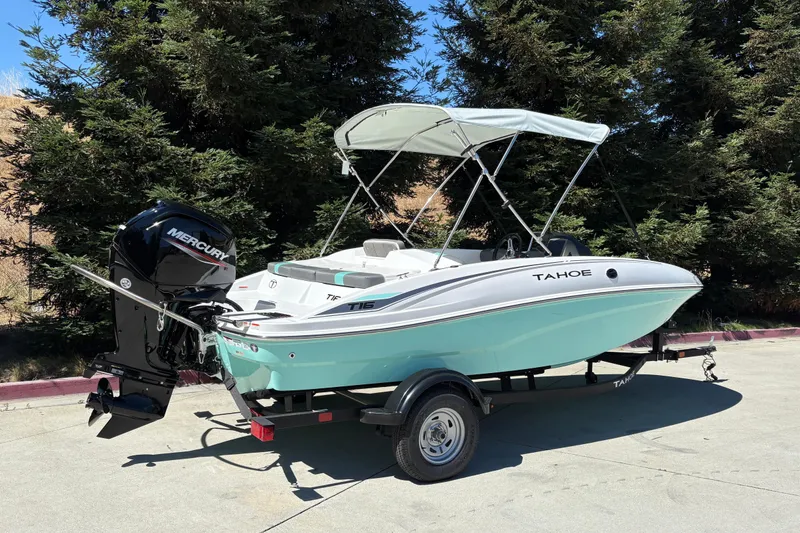 Slide: The Image of 2026 Tahoe T16 boat with Mercury engine, parked on a trailer, surrounded by trees. - 1