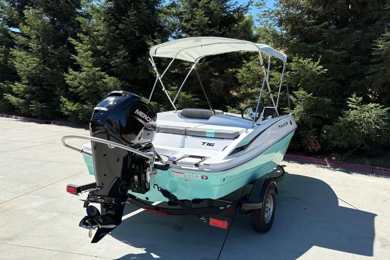 Slide: The Image of 2026 Tahoe T16 boat with Mercury engine, parked outdoors, surrounded by trees. - 9