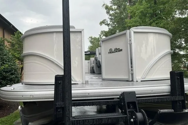 Slide: The Image of 2026 Sun Tracker Party Barge 22 DLX pontoon boat on trailer, surrounded by greenery. - 100