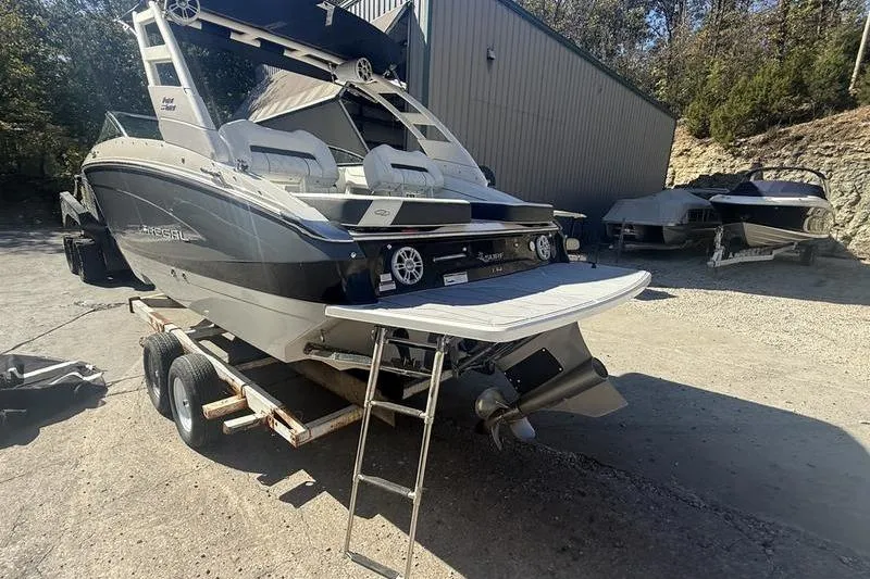 Slide: The Image of 2023 Regal LS4 Surf boat on trailer, parked outdoors near a building. - 6