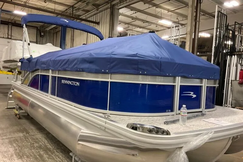 Slide: The Image of 2026 Bennington 22SXSR pontoon boat with blue cover in a warehouse setting. - 10