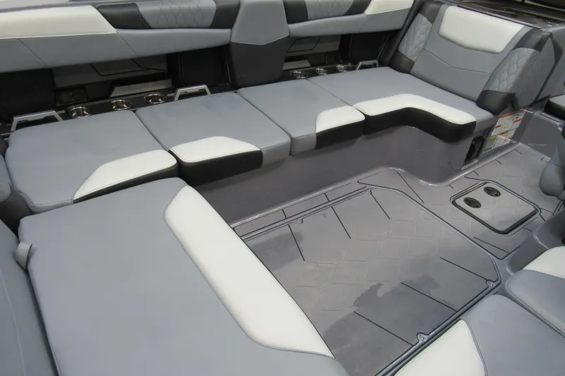 Slide: The Image of 2024 Malibu M220 boat interior with gray and white seating, cup holders, and textured flooring. - 5