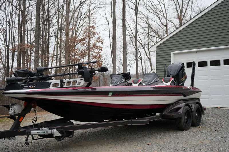 The Image of 2021 Skeeter FXR21 Apex boat on trailer near garage, surrounded by trees. - 0