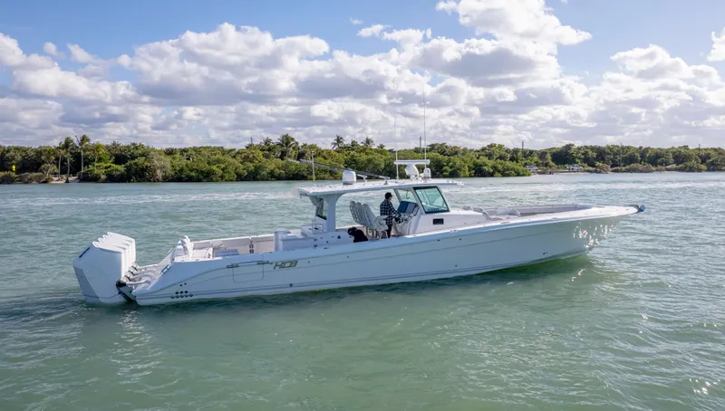 Slide: The Image of 2024 HCB 53' Suenos boat cruising on a sunny day, surrounded by lush greenery. - 10