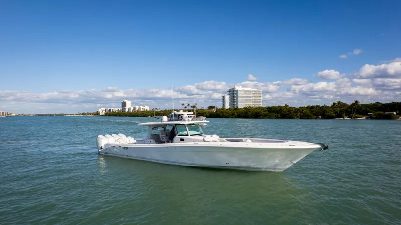 Slide: The Image of 2024 HCB 53' Suenos boat cruising on a sunny day with buildings in the background. - 2