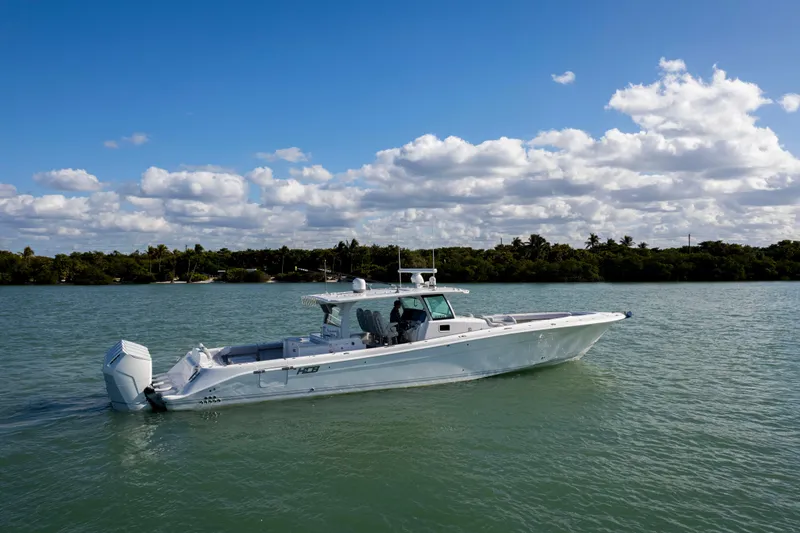 Slide: The Image of 2024 HCB 53' Suenos boat cruising on a calm, scenic waterway under a blue sky. - 2