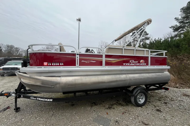 Slide: The Image of 2025 Sun Tracker Bass Buggy 18 DLX pontoon boat on trailer, parked outdoors. - 18