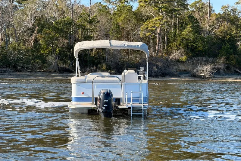 Slide: The Image of 2021 SunCatcher Select 20C pontoon boat on a calm lake near a forested shoreline. - 4