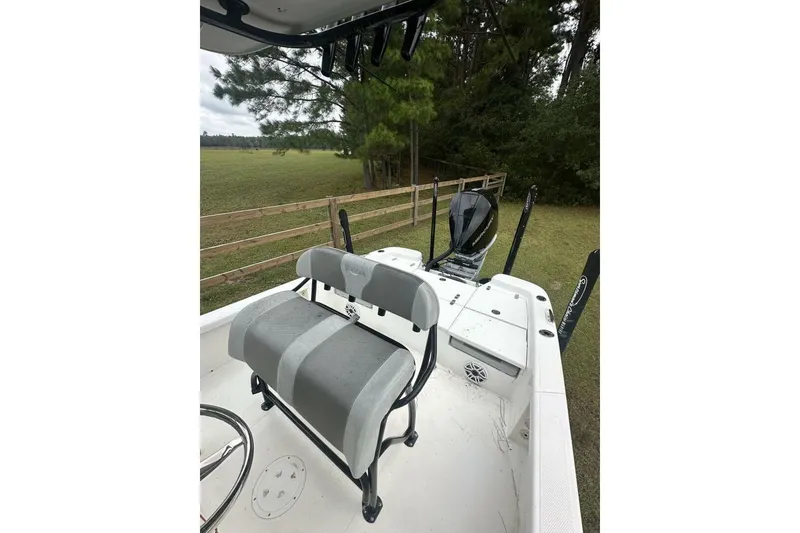 Slide: The Image of 2022 BlackJack 256 Bay boat interior with seating and motor, set in a grassy area. - 6